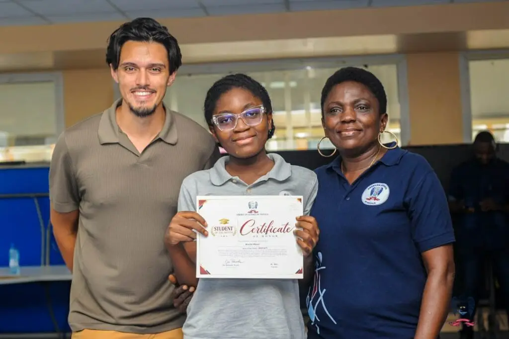 Young ASD student proudly displays a Student of the Month certificate alongside two adults during the October awards.