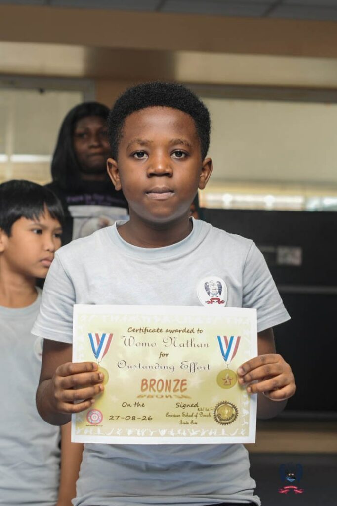Young student at American School of Douala proudly displays an October Student of the Month achievement certificate.