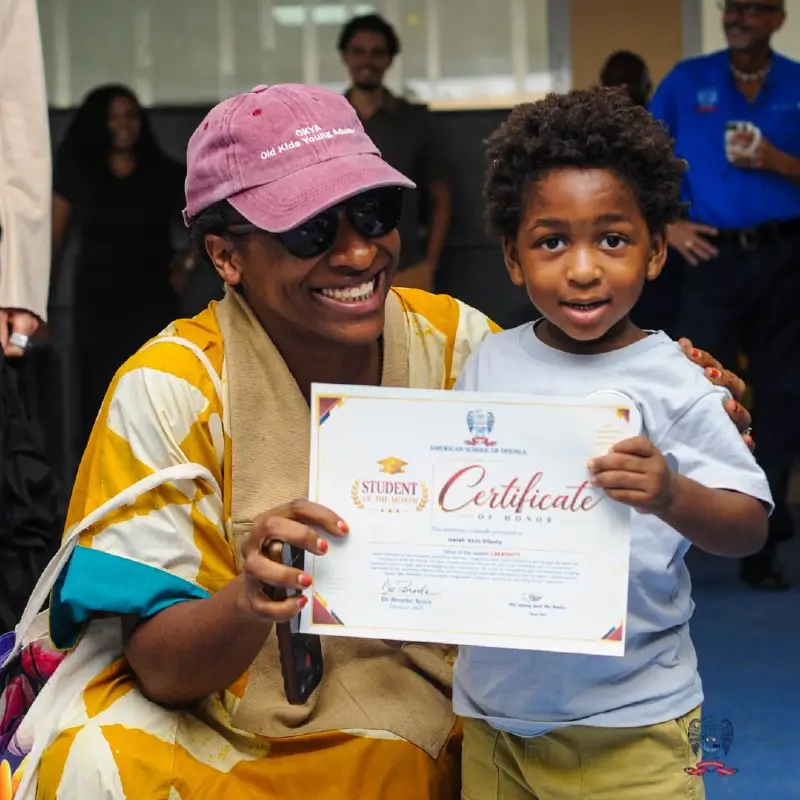 Young student displays an October Student of the Month certificate alongside an adult at American School of Douala.